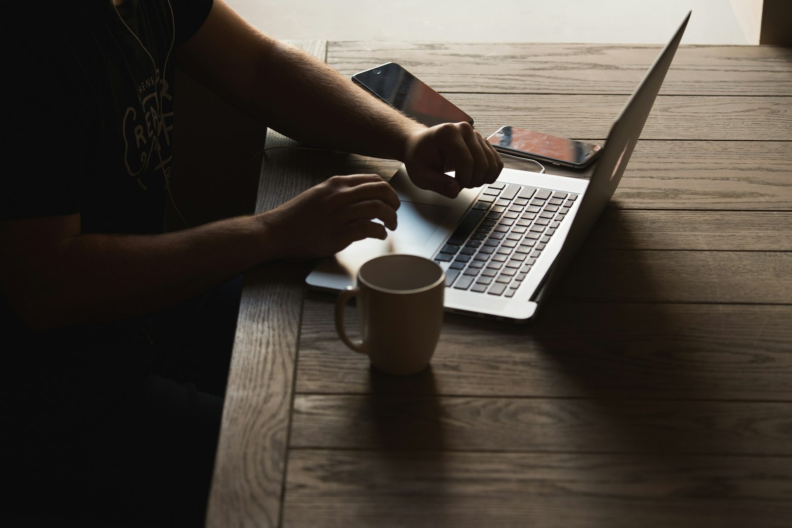 Grey laptop on a wooden table, a person seated on the chair beside it